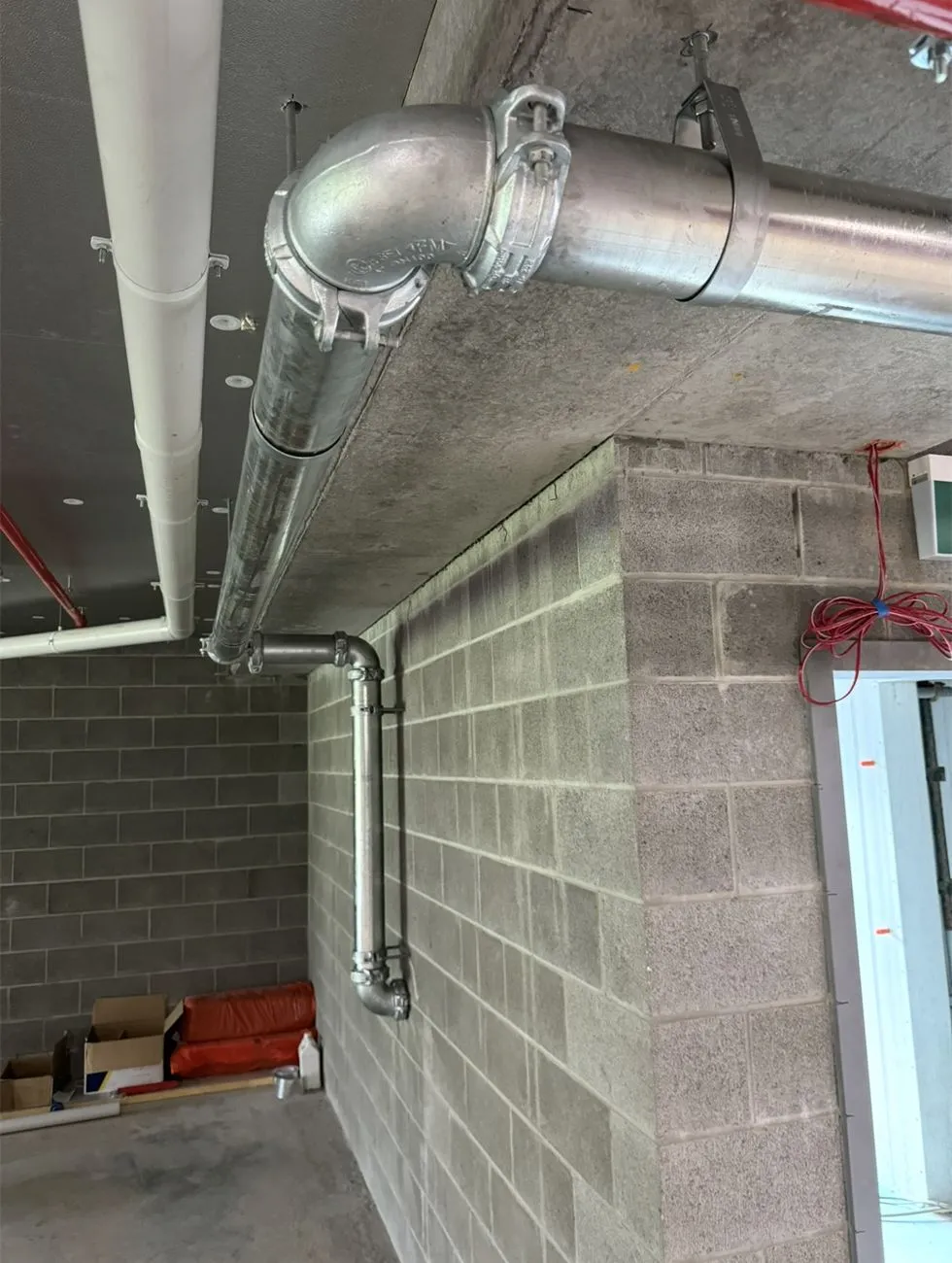 Galvanised commercial pipework along a block wall